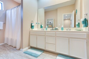 A bathroom with a large mirror, white cabinets, a shower curtain, and a blue rug.