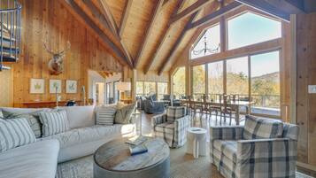 A spacious living area with a wooden ceiling, large windows, and a mounted deer head.