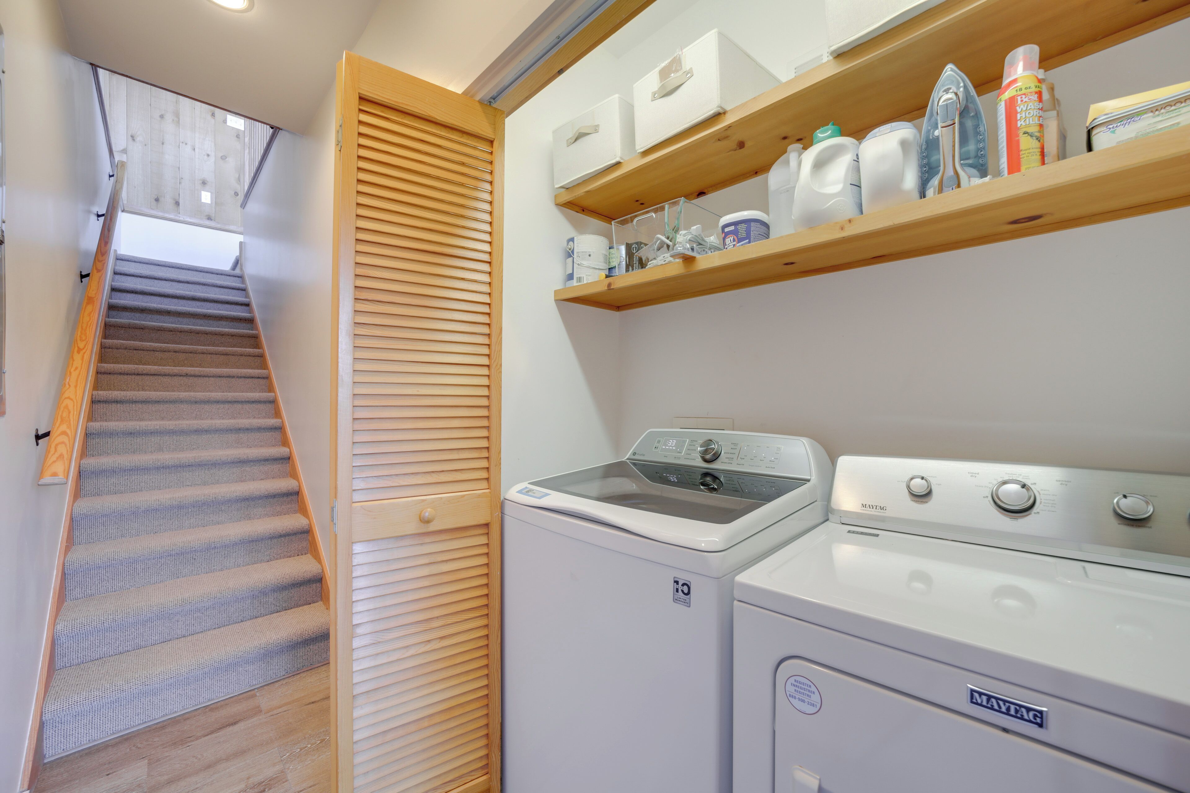A laundry area with a washing machine, dryer, and shelves above containing cleaning supplies.