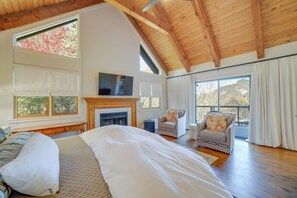 A spacious bedroom with a large bed, a fireplace, a television, and a balcony with curtains. - Mountain-view Cashiers Home: Near High Hampton!- (Cashiers)