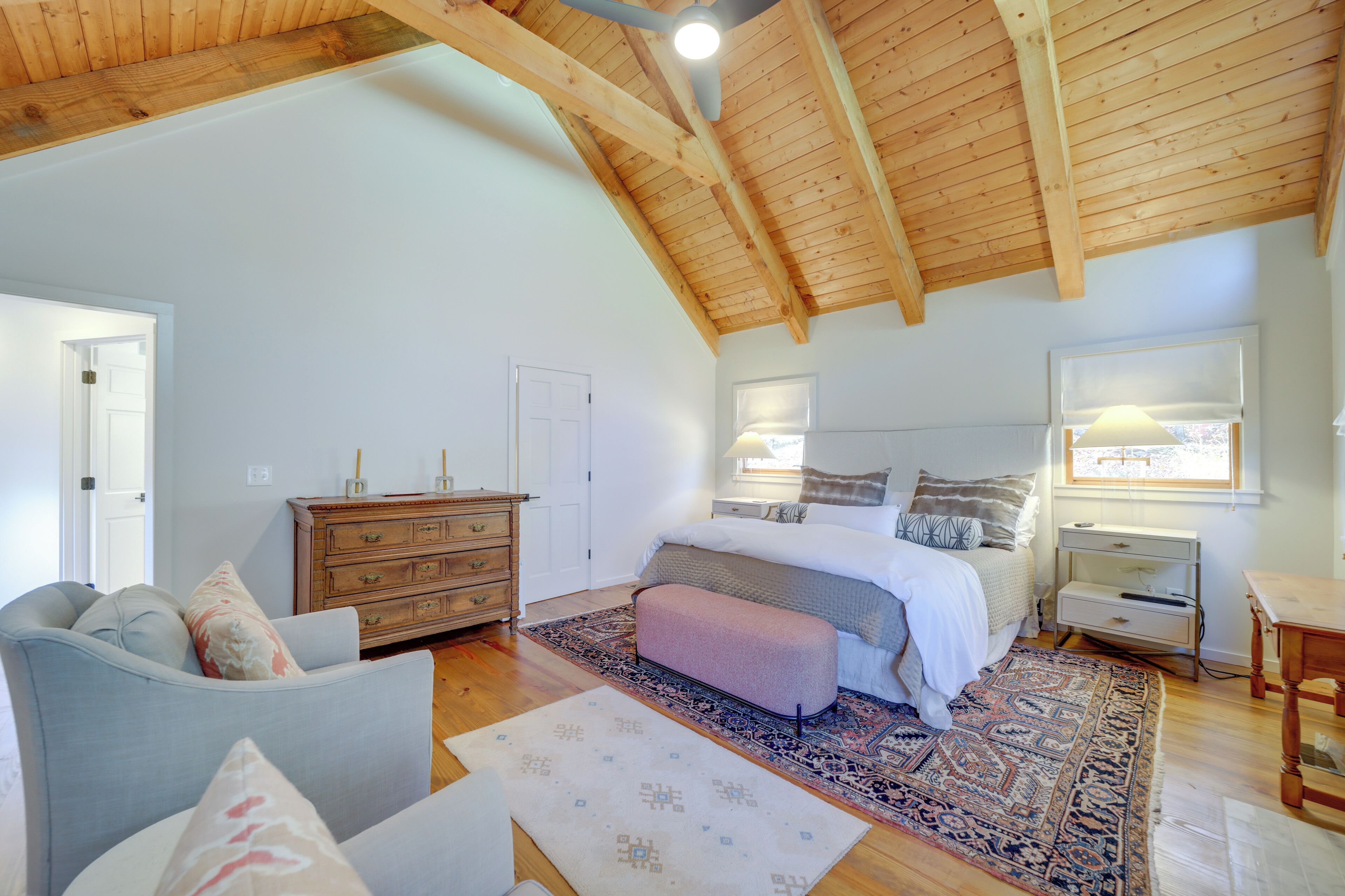 Ein Schlafzimmer mit einem großen Bett, Holzboden, einem Schminktisch, einem Nachttisch und einem Fenster mit Blick.