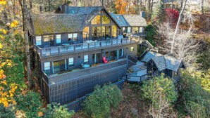 A large, multi-story cabin with a deck and outdoor seating area, surrounded by trees and autumn foliage. - Mountain-view Cashiers Home: Near High Hampton!- (Cashiers)