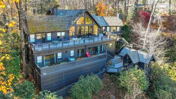 A large, multi-story cabin with a deck and outdoor seating area, surrounded by trees and autumn foliage.