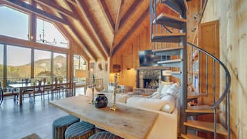 A spacious wooden interior with a dining area, a fireplace, and a spiral staircase.