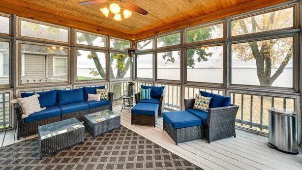 A covered outdoor seating area with a wooden ceiling, large windows, and wicker furniture. - Lakefront Edgerton Cottage w/ Deck & Grill! (Edgerton)