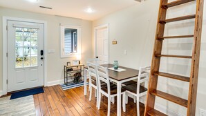 A dining area with a wooden table and white chairs, a ladder, and a small side table with a lamp. - Lakefront Edgerton Cottage w/ Deck & Grill! (Edgerton)