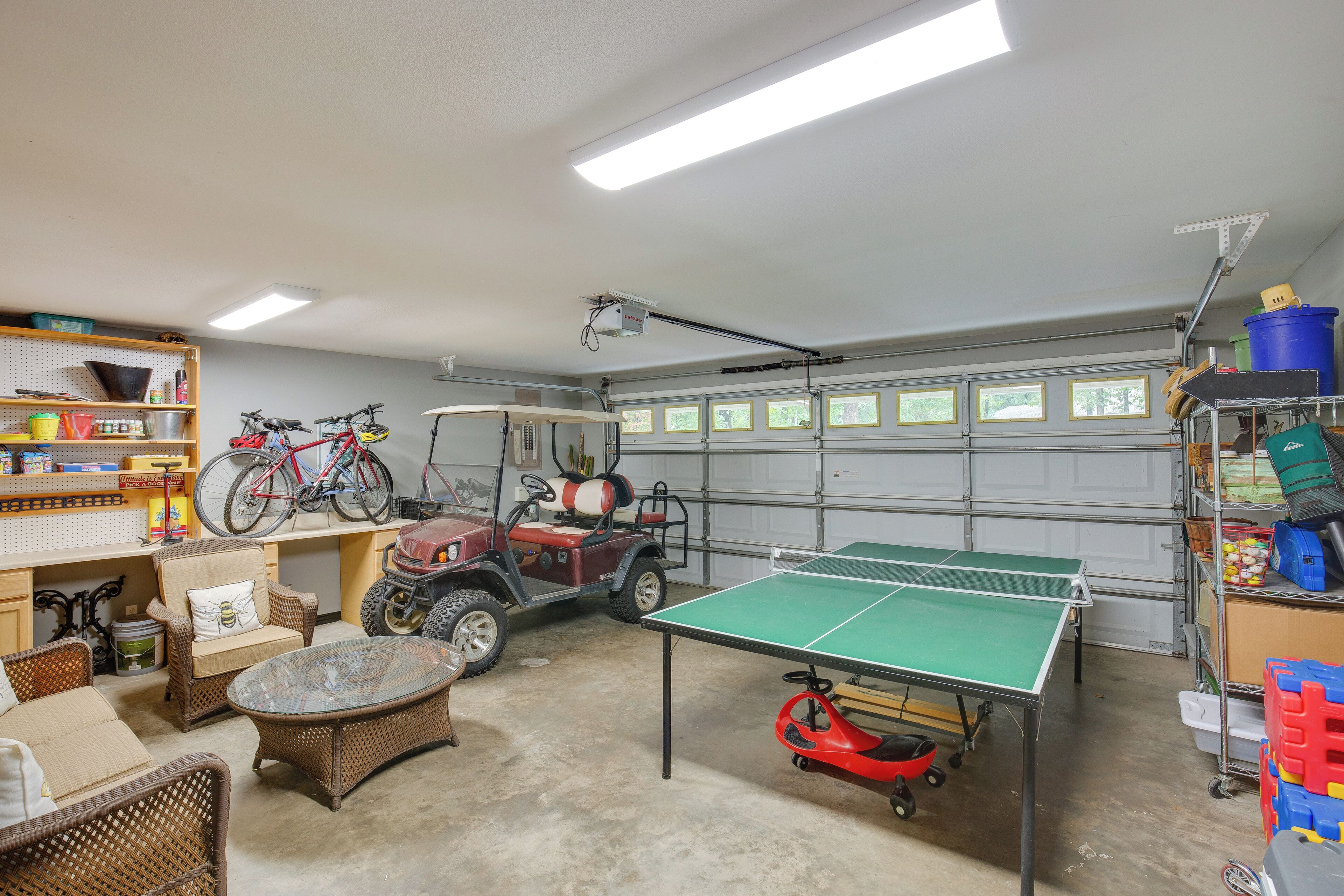A garage with a ping pong table, wicker furniture, bicycles, and a golf cart.