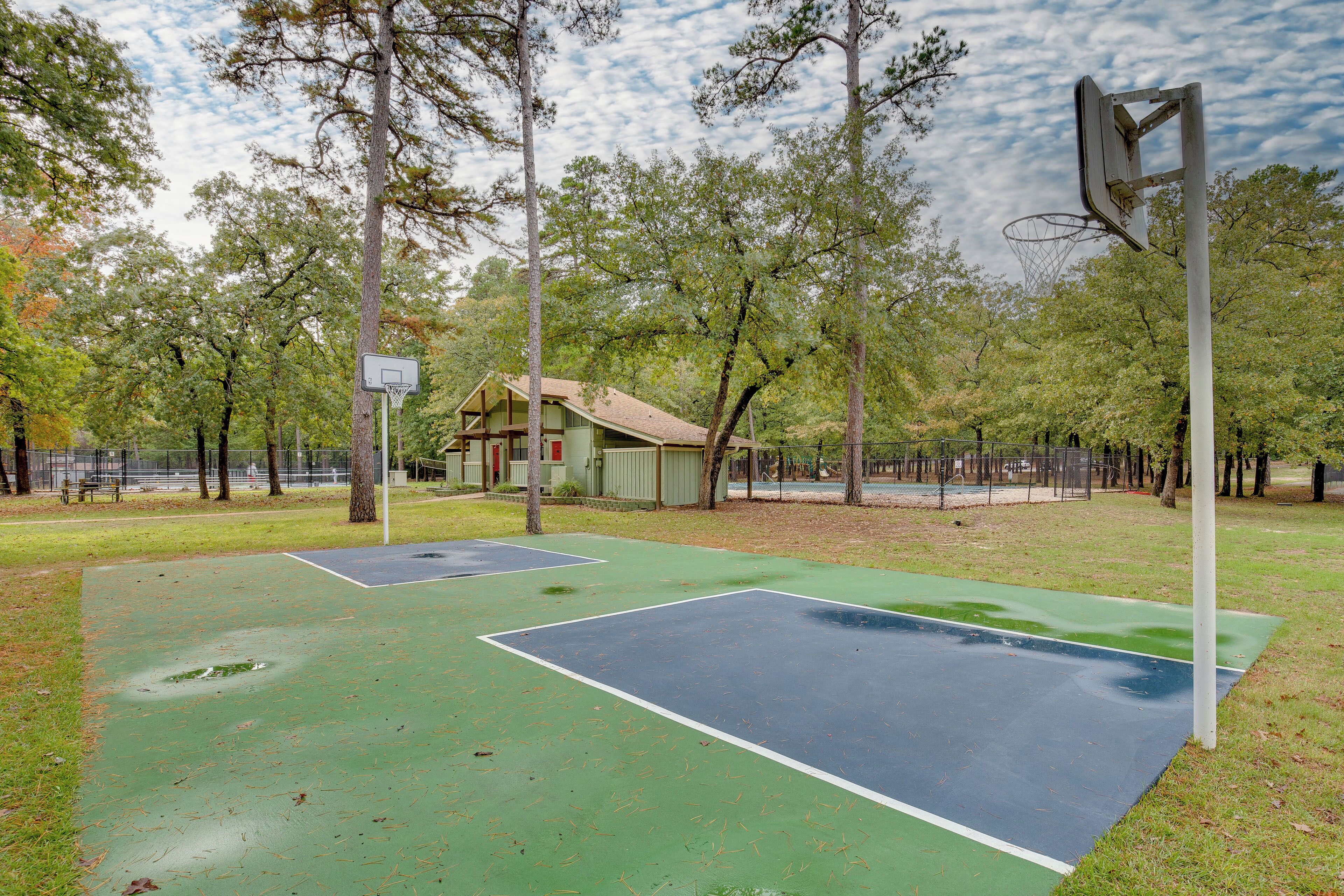 An outdoor basketball court with two courts, surrounded by trees and a building in the background.