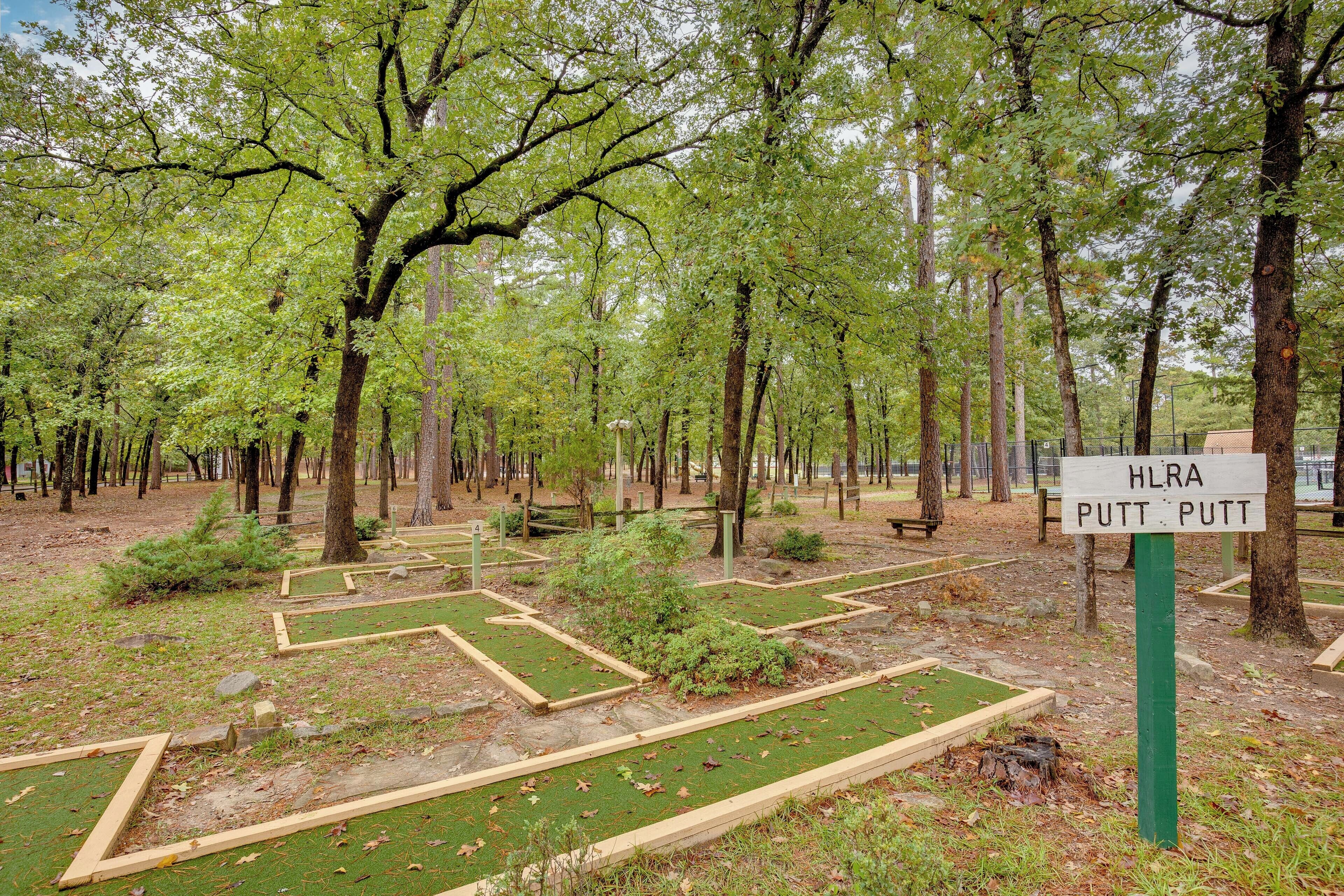 Un parque con un cartel que dice 'HLRA PUTT PUTT' y una zona laberíntica con césped verde y marcos de madera.
