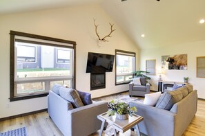 A spacious living room with large windows, a fireplace, and a mounted deer antler. - Pet-friendly Bozeman Home ~ 7 Mi to Downtown! (Bozeman)