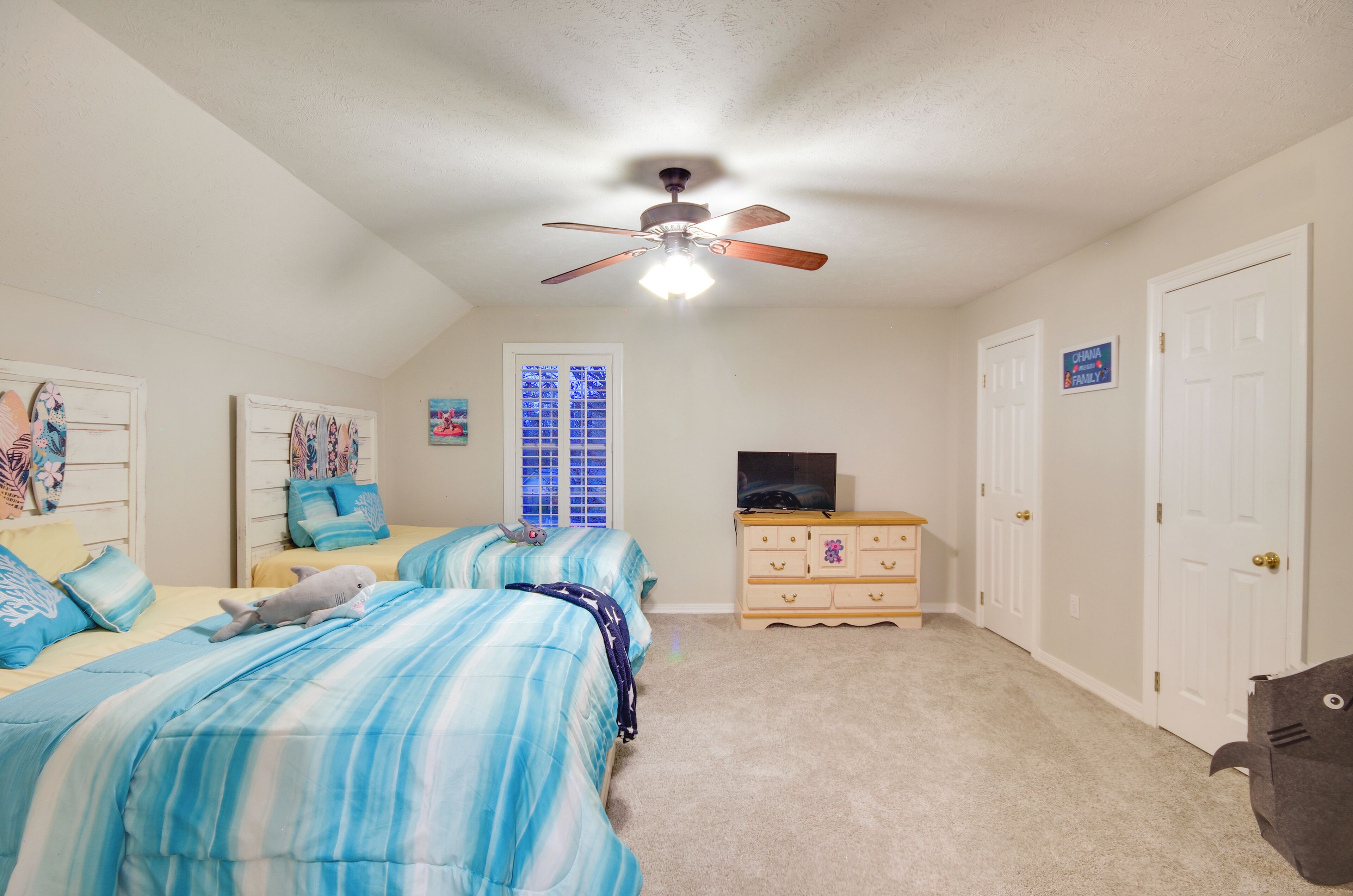 A bedroom with two beds, a ceiling fan, a dresser, and a television.
