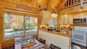 Una cocina acogedora de estilo cabaña con armarios de madera, una isla central y un amplio ventanal con vistas a un bosque.