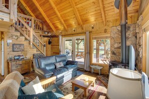 L’intérieur chaleureux d’un chalet avec un escalier en bois, un canapé en cuir noir, une cheminée en pierre et un coin repas.