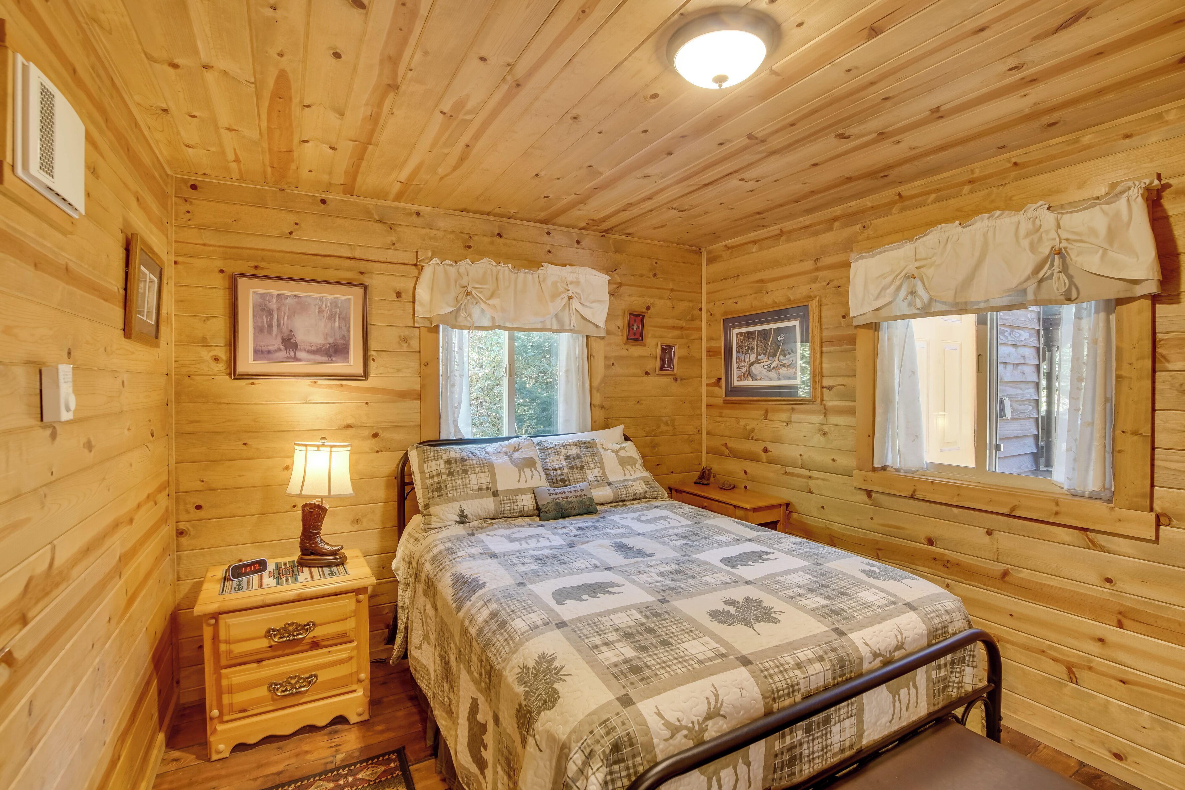 A wooden cabin bedroom with a bed, nightstands, and framed pictures on the walls.