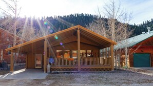 Een houten lodge met een overdekte veranda, een groene garage en een bergachtige achtergrond.