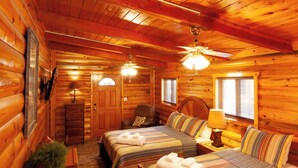 Een blokhutkamer met twee bedden, een houten plafond en een plafondventilator.