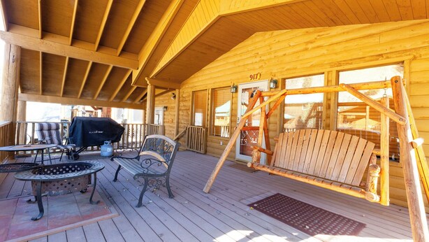 Een houten terras met een schommel, een barbecue en buitenmeubels.