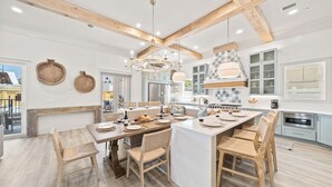 Een ruime keuken met houten balken, een centraal eiland en een eethoek met rieten stoelen.