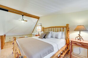 Cozy bedroom with a sloped ceiling, featuring a central bed with a wooden headboard and a nightstand with a lamp.