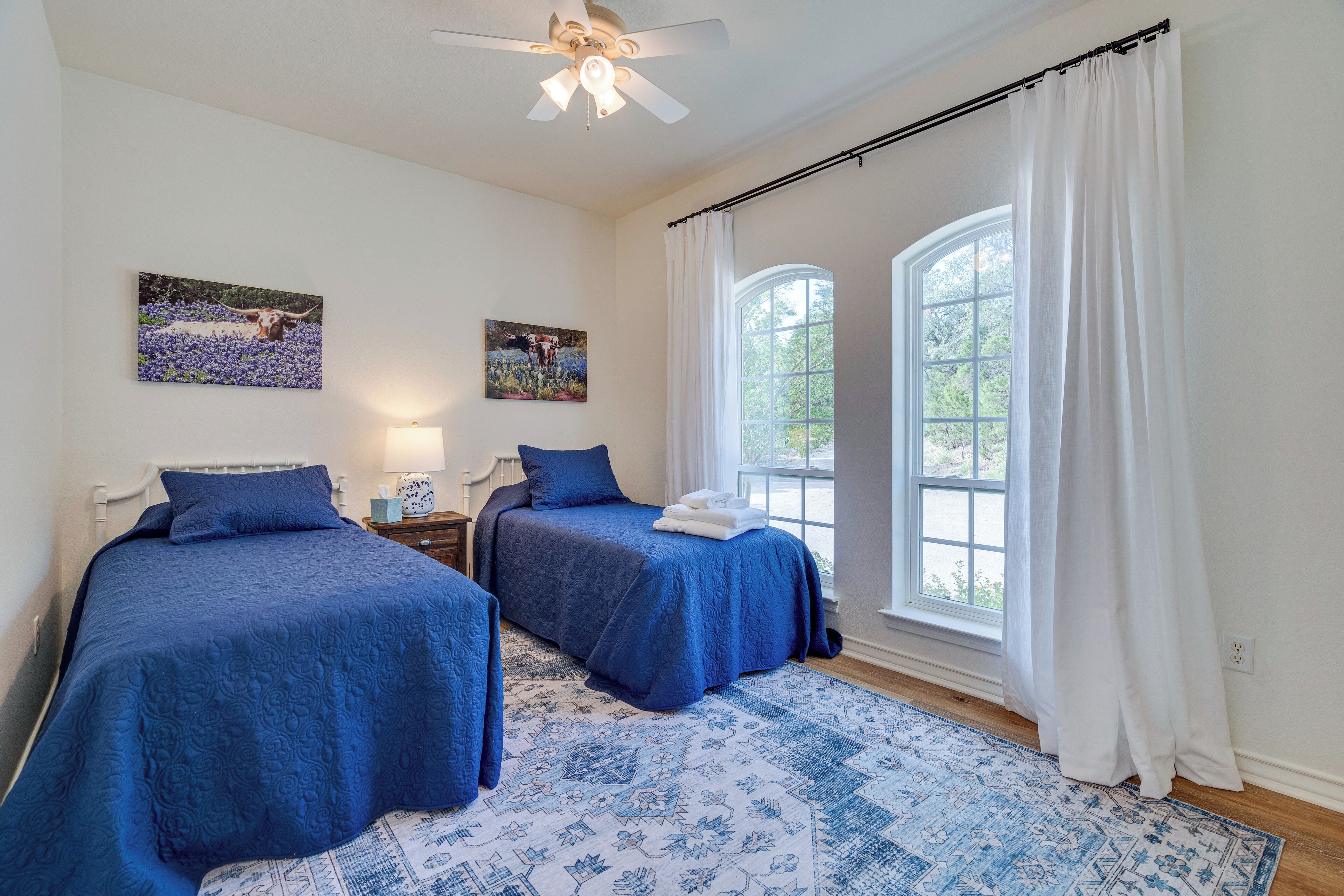 A bedroom with two beds, a ceiling fan, and large windows with white curtains.