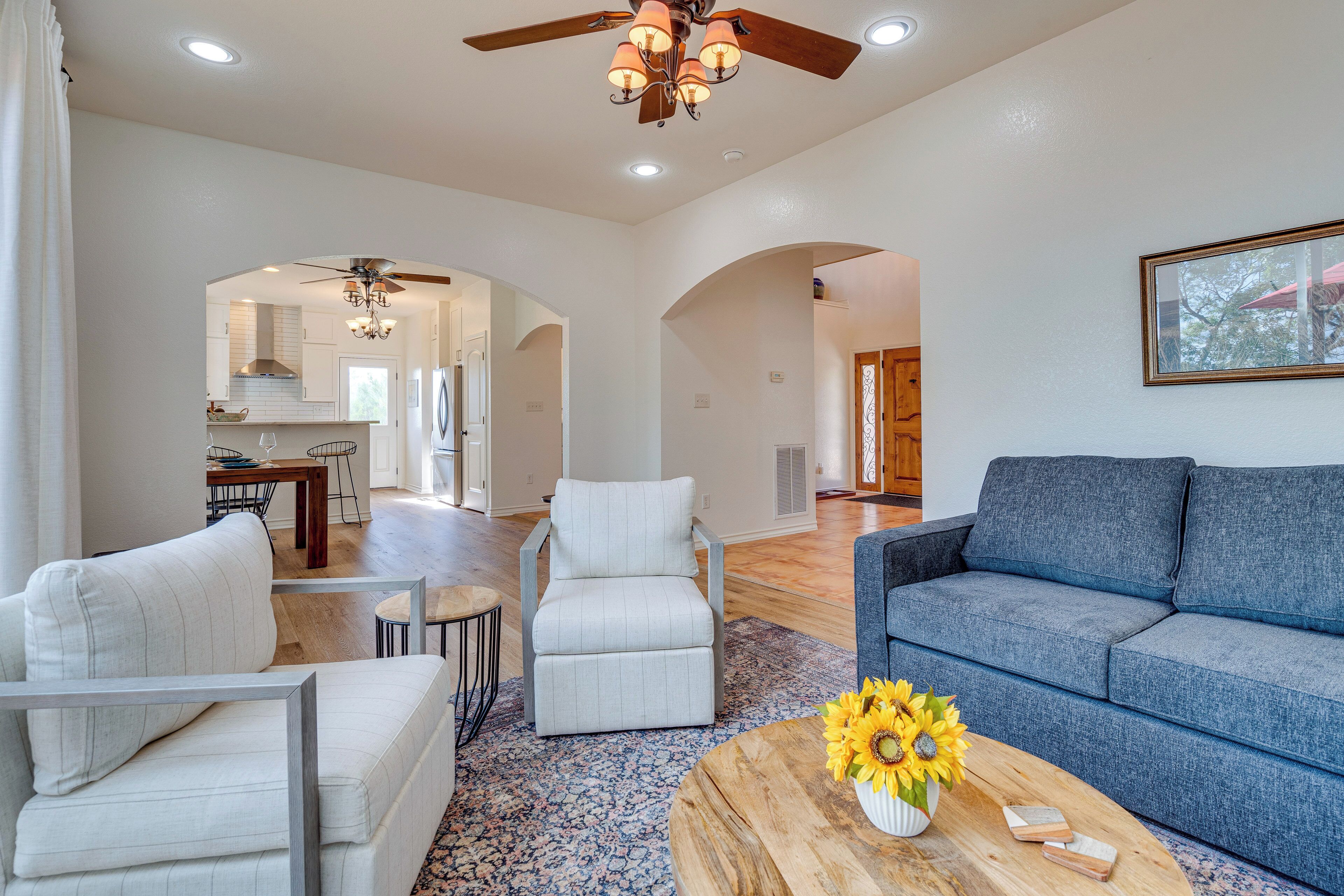 A spacious living room with a blue sofa, white armchairs, and a coffee table with sunflowers.