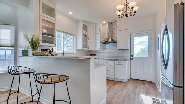 A modern kitchen with white cabinetry, a central island, two bar stools, and a stainless steel refrigerator. - Jonestown Retreat w/ Deck: 6 Mi to Lake Travis! (Leander)