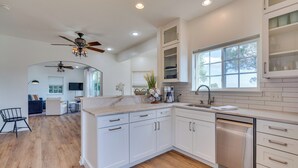 A modern kitchen with white cabinets, a dishwasher, and a large window. - Jonestown Retreat w/ Deck: 6 Mi to Lake Travis! (Leander)