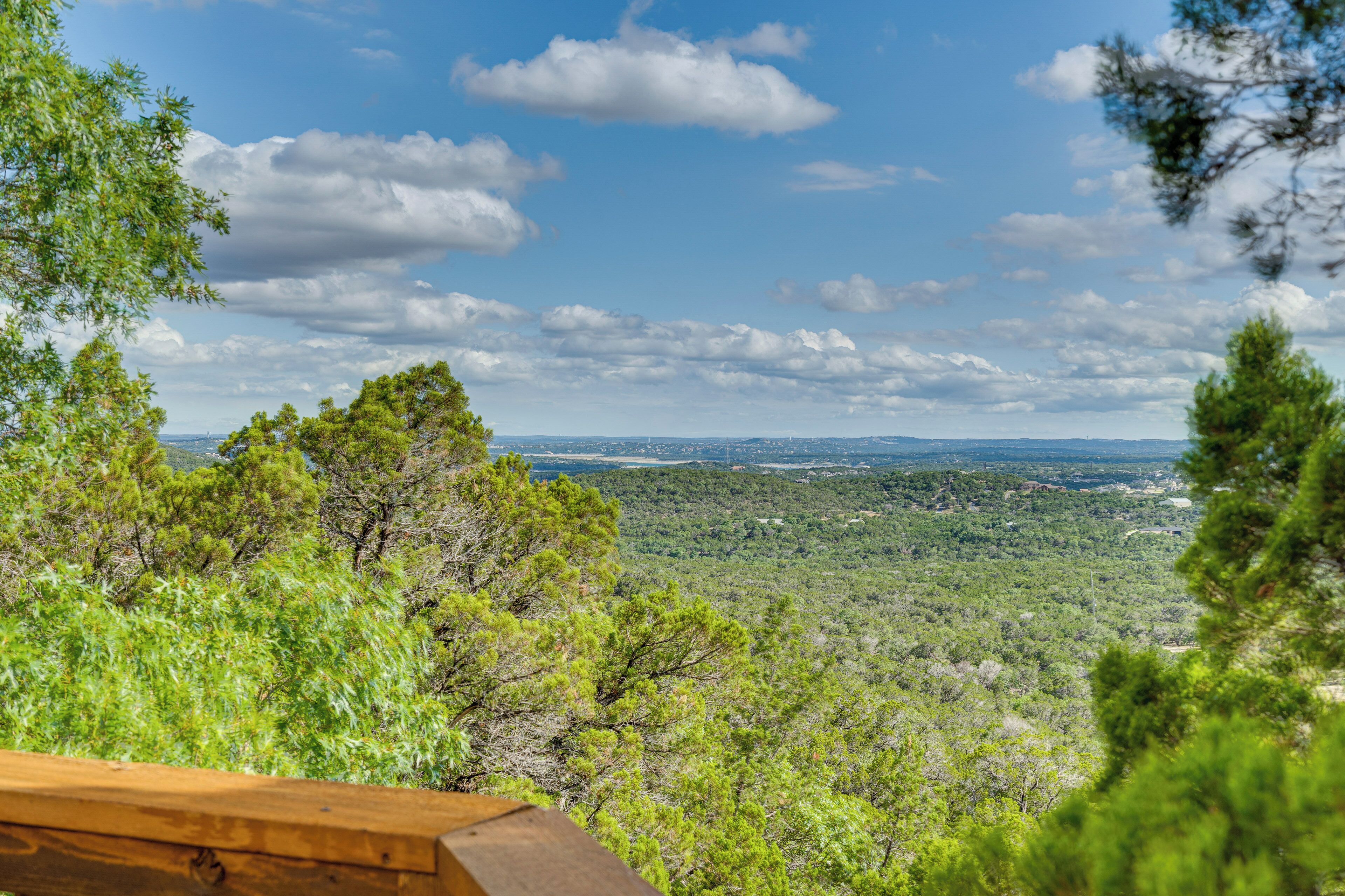 Une vue depuis une terrasse en bois donnant sur un paysage boisé, avec des collines qui se dessinent à l’horizon.