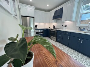 A modern kitchen with white and dark blue cabinets, stainless steel appliances, and a wooden countertop.