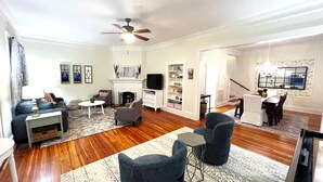 A spacious living room with a fireplace, a dining area, and a staircase leading to another level. - Historic district- yard, putting green, firepit (Saint Augustine)
