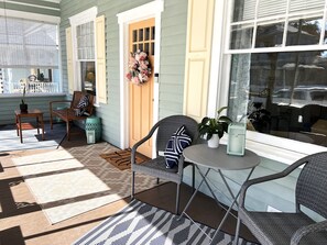 A sunlit porch with wicker furniture, a small table, and a potted plant.