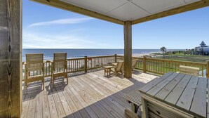 Eine Holzterrasse mit Stühlen und Tisch mit Blick auf einen Strand.