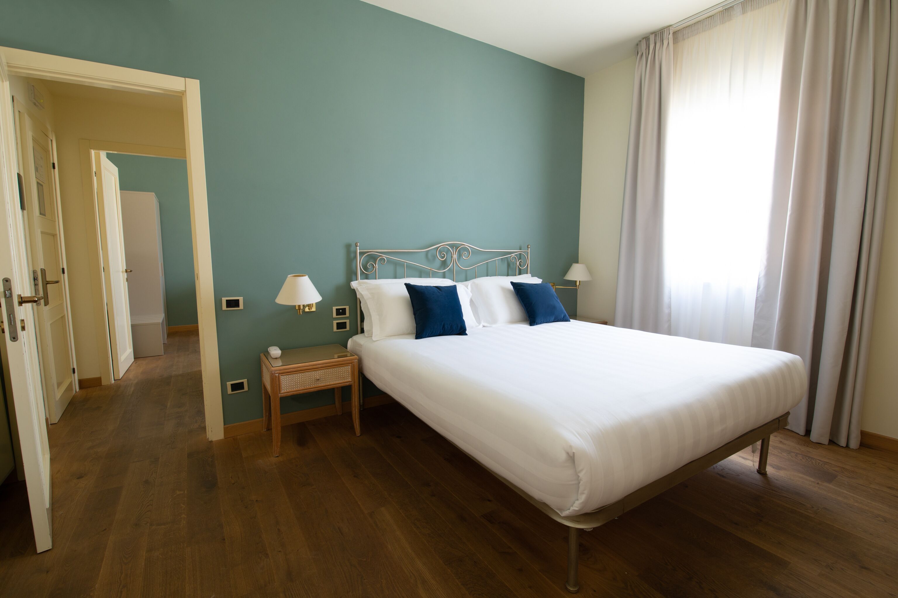 A bedroom with a single bed, a bedside table, a lamp, and a window with curtains.