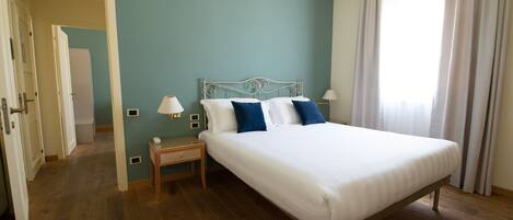 A bedroom with a single bed, a bedside table, a lamp, and a window with curtains.