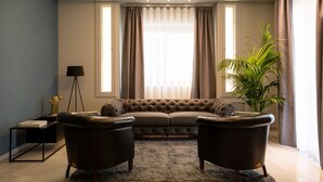 A living room with a tufted sofa, two armchairs, a floor lamp, a potted plant, and a large window with curtains. - Hotel Enzo (Porto Recanati)