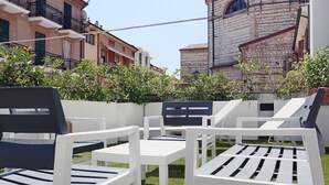 Outdoor seating with white and black chairs, a white table, and a brick building in the background. - Hotel Enzo (Porto Recanati)