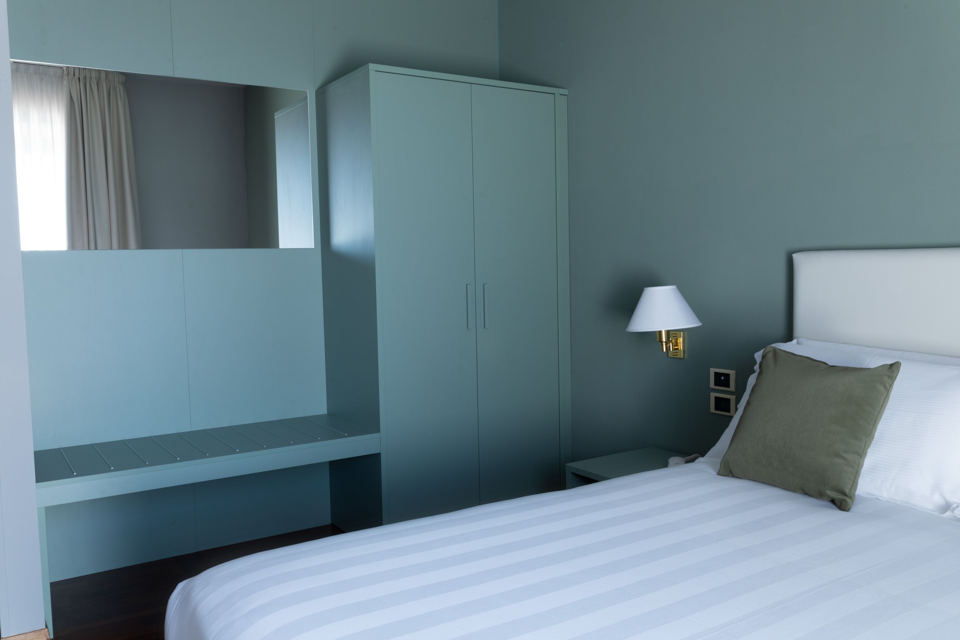 Una habitación de hotel con cama, armario, mesita de noche y lámpara.
