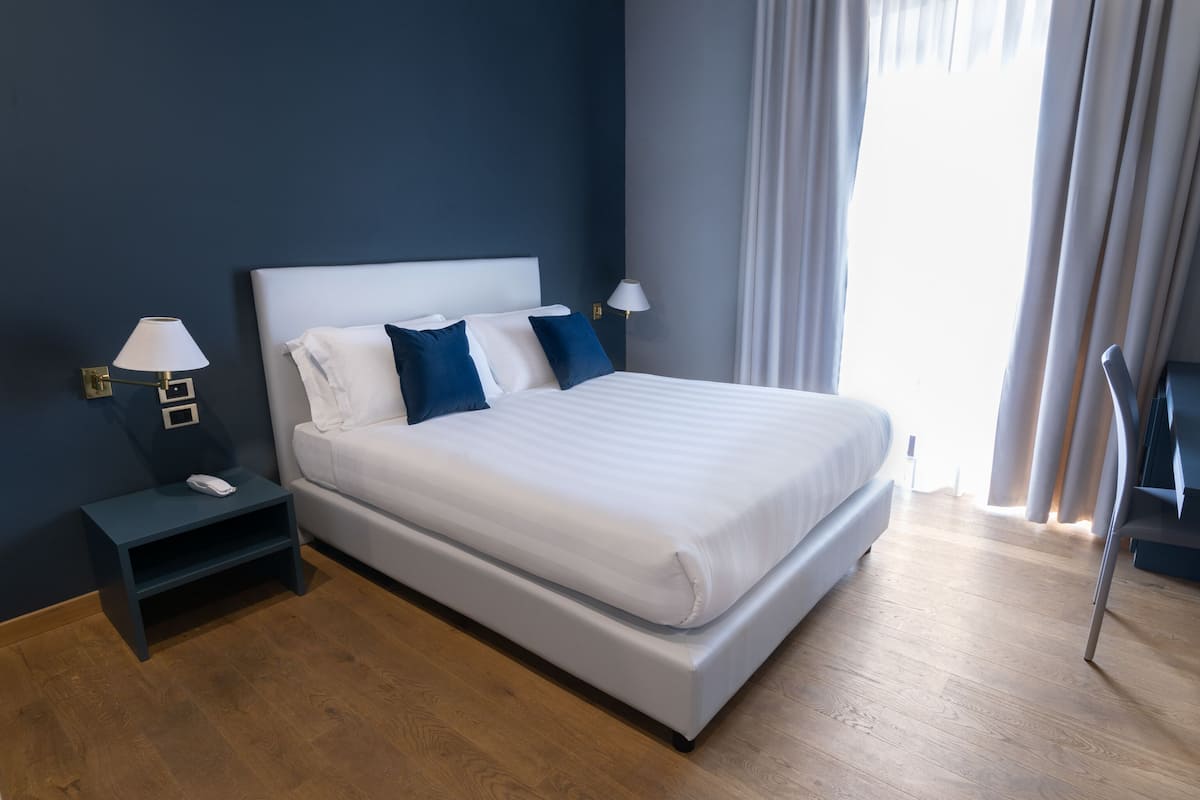Una habitación de hotel moderna con una cama grande, mesitas de noche y vistas al exterior.