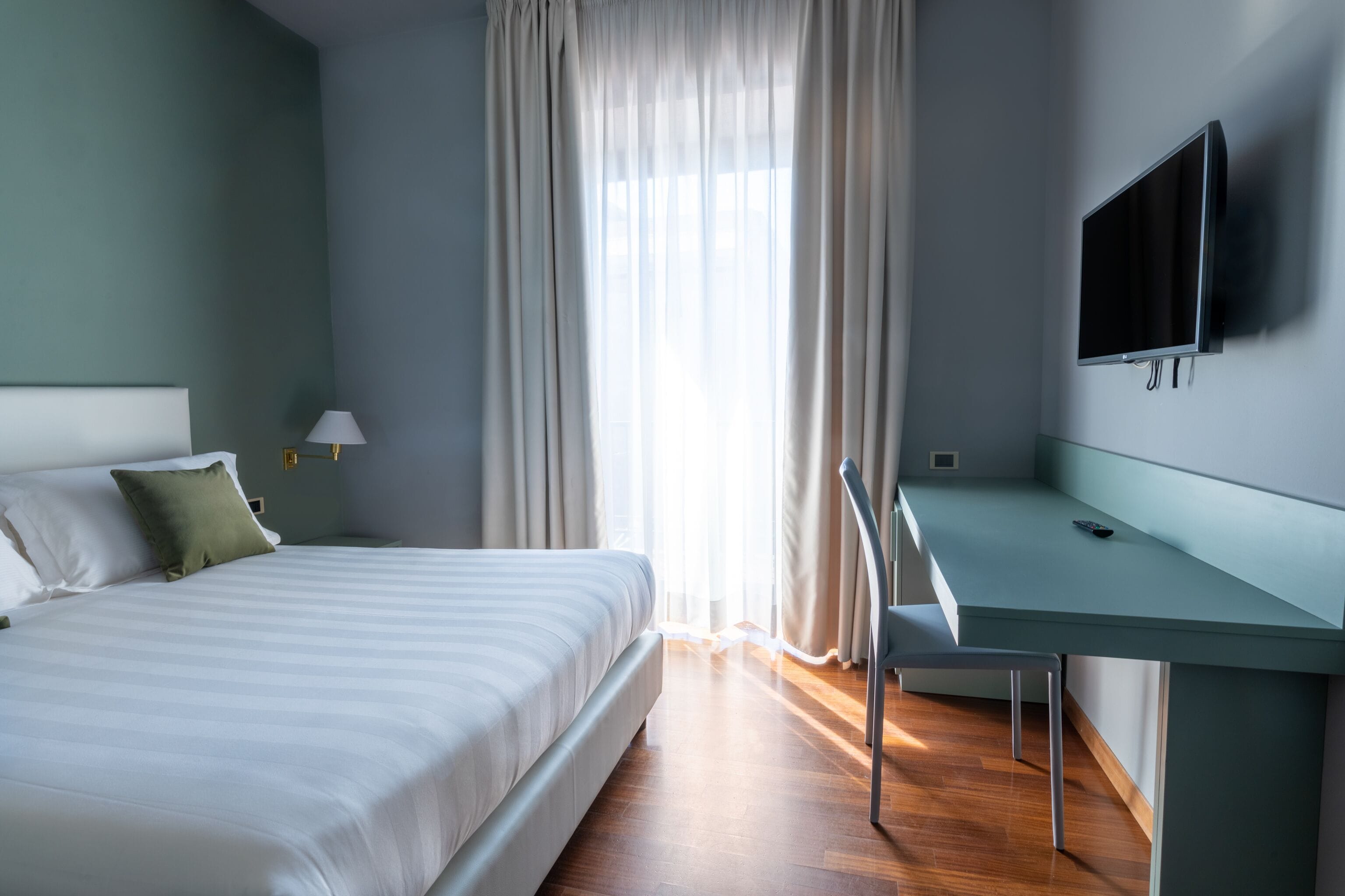 Una habitación de hotel moderna con una cama, un escritorio y un televisor montado en la pared.