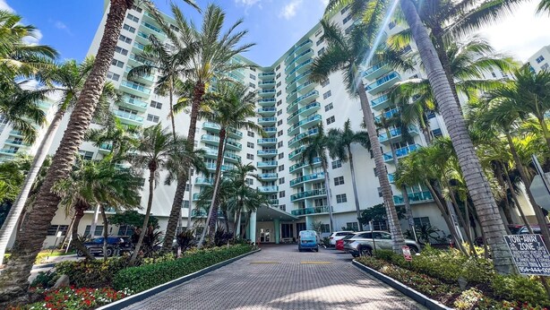 A multi-story hotel with a central entrance, surrounded by palm trees and a paved walkway. - Beachfront Apt | Tides Hollywood 5th Floor + Pool (Hollywood)