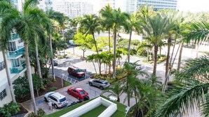 A parking area with multiple cars, palm trees, and a building with a modern design. - Beachfront Apt | Tides Hollywood 5th Floor + Pool (Hollywood)