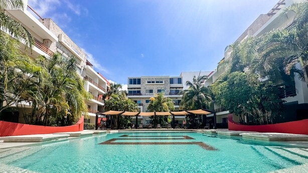 A swimming pool with clear water, surrounded by palm trees and a building with balconies. - Sabbia 2310- 3bedrooms all in Suite (Playa del Carmen)