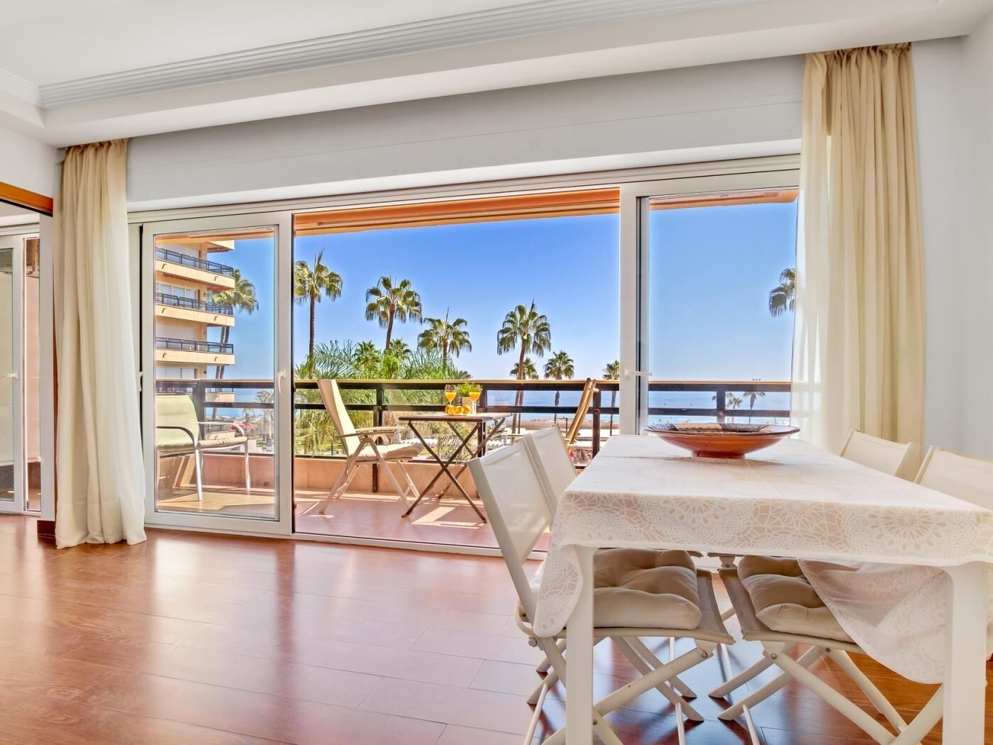 Un balcón con mesa, sillas y vistas a palmeras y al mar.