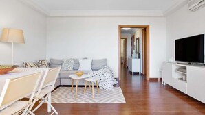Ett modernt vardagsrum med en soffa, ett matbord, en tv och en hall som leder till ett kök.