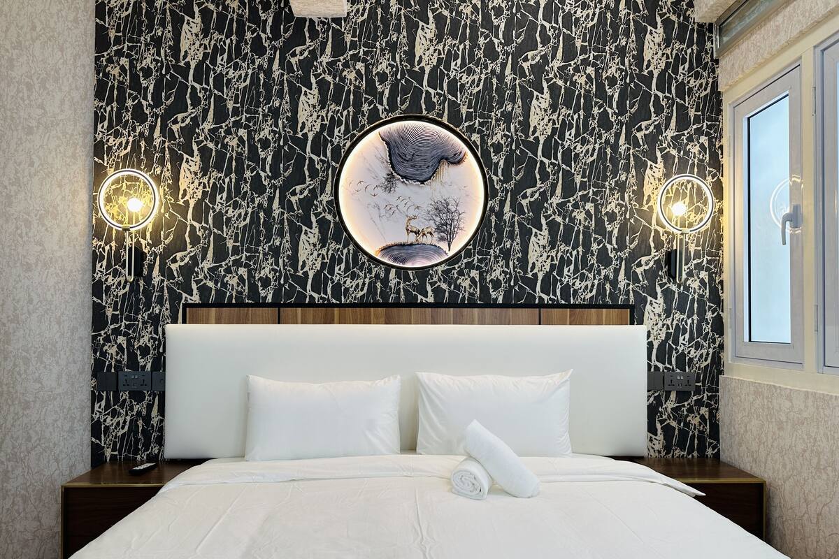 A hotel room with a marble-patterned wall, a round mirror, and two wall sconces.
