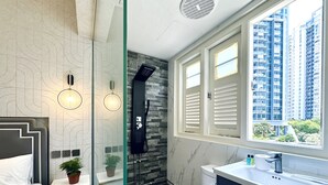 A modern bathroom with a glass shower enclosure, a white toilet, a sink with a mirror, and a window with blinds. - KAM LENG HOTEL (Singapore)