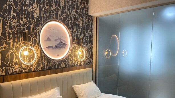 A modern bedroom with a bed, two bedside tables, and a wall with circular light fixtures. - KAM LENG HOTEL (Singapore)