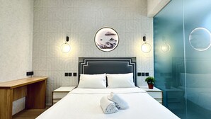 A modern hotel room with a large bed, two bedside tables, a wooden bench, a round mirror, and wall sconces. - KAM LENG HOTEL (Singapore)