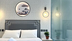 A modern hotel room with a large bed, a circular wall art piece, two wall-mounted lights, and a small potted plant on the nightstand. - KAM LENG HOTEL (Singapore)