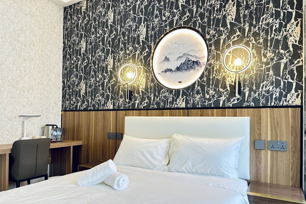 A hotel room with a bed, a desk, and two wall-mounted lights.
